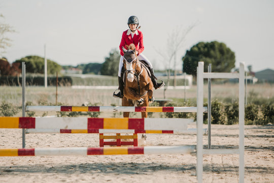 Teenage jockey on horse leaping over horizontal wooden bars while riding on racetrack
