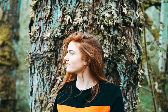 Redhead woman standing against tree trunk
