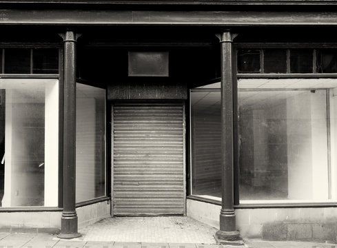monochrome facade of an old abandoned shop with empty store front dirty windows and closed shutters on the door