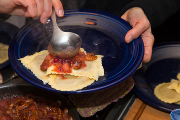 Woman ladling pecan and cranberry sauce on pierogi dumplings. St Paul Minnesota MN USA