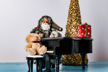 grey clad Santa Claus leaning against piano with stuffed bear sitting on bench