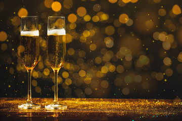 Glasses of champagne and golden glitter on table against blurred background. Space for text
