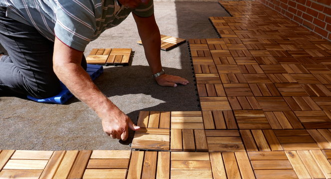 A craftsman is laying wooden tiles on a terrace. It connects square wood panels with Lock Clic