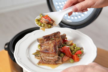 Woman putting meat and garnish prepared in multi cooker on plate, closeup