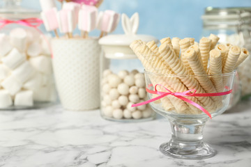 Vase with wafer rolls and other sweets on white marble table, space for text. Candy bar
