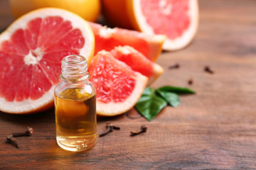 Bottle of essential oil and fresh grapefruit on wooden table, space for text