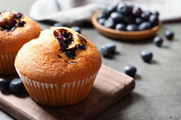 Wooden board with blueberry muffins on grey table, closeup view. Space for text