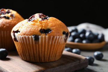 Wooden board with blueberry muffins on grey table against black background, closeup view. Space for...