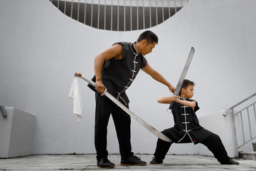 Father and son are engaged in Wushu in the city. The photo illustrates a healthy lifestyle and sport. The father trains the son.