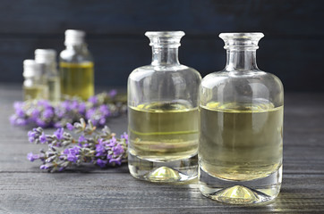 Obraz na płótnie Canvas Bottles with natural lavender oil and flowers on grey wooden table against dark background, closeup view. Space for text