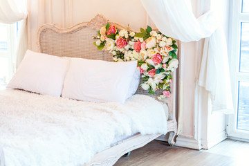 Beautiful luxury classic white bright clean interior bedroom in baroque style with king-size bed, large window, armchair and flower composition