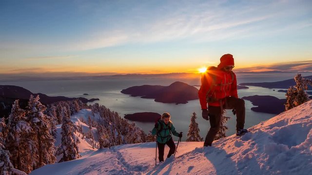 Adventure seeking man and woman are hiking to the top of a mountain during a vibrant winter sunset. Taken in Mount Harvey, North of Vancouver, BC, Canada. Still Image Continuous Animation