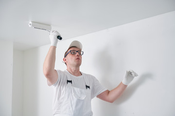 Painter worker with roller painting ceiling surface into white