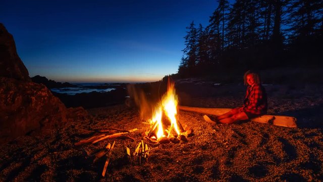 Girl enjoying a camp fire on the beach during a vibrant summer sunset. Taken in Northern Vancouver Island Ocean Coast, BC, Canada. Still Image Continuous Animation