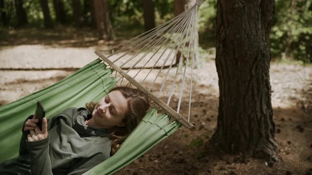 Happy girl resting on a hammock using a smart phone on vacation