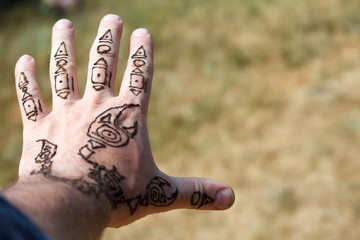 Arabic mehendi scorpion drawing on a mans hand on a blurred background of meadows, selective focus