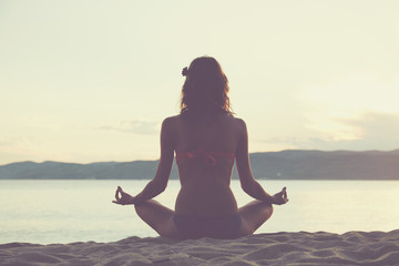 Young woman practicing yoga on the sandy beach.
