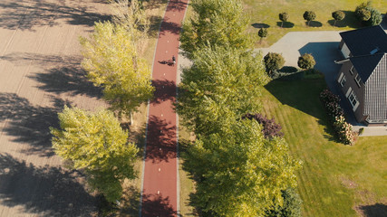 Aerial view of a bicycle highway in The Netherlands in a suburban environment with tall autumn trees casting long shadows along the side and bikers passing by