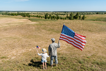 back view of military man and patriotic kid holding american flags