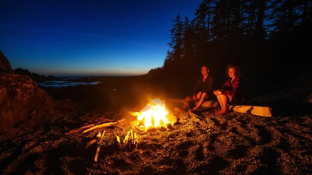 Couple friends are enjoying a camp fire on the beach during a vibrant summer sunset. Taken in Northern Vancouver Island Ocean Coast, BC, Canada. Still Image Continuous Animation