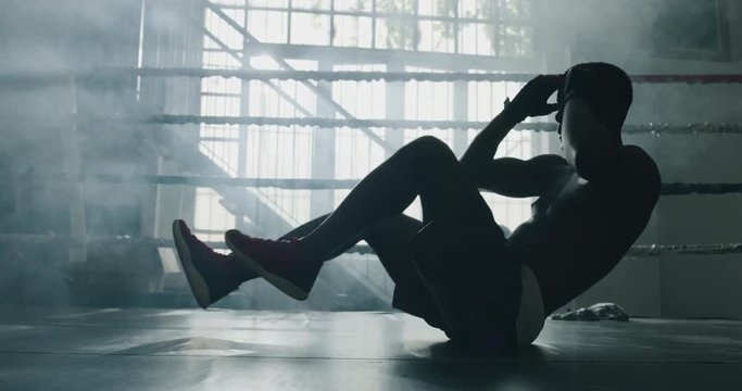 Cinematic shot of a professional young muscular shirtless african man is practicing shadow boxing work out in a gym with ring. 