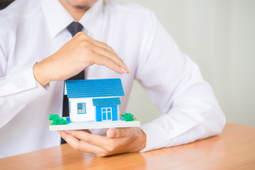 Home insurance concept. Businessman with house miniature