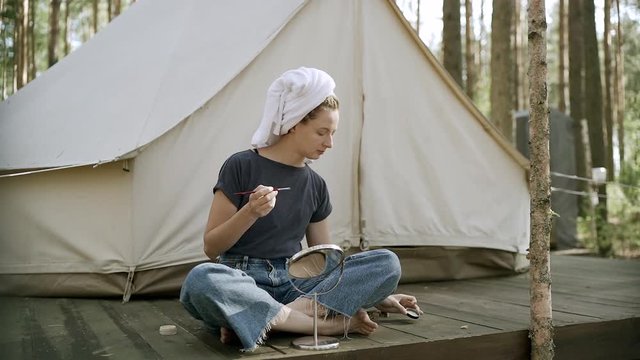 Woman doing make up near tent in the forest.