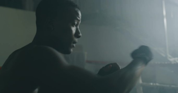 Cinematic slow motion shot of a professional young muscular shirtless african man is practicing shadow boxing work out in a gym with ring. 
