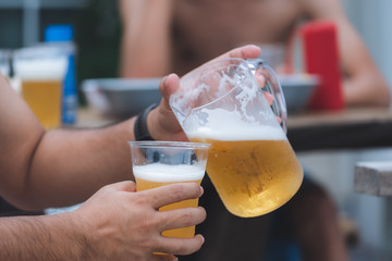 Close up hands of unidentified man pouring beer from pitcher to plastic glass at home yard