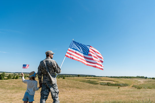 soldier holding hands with kid in straw hat and holding american flag
