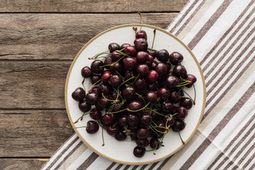 top view of fresh, whole and ripe cherries covered with droplets on plate