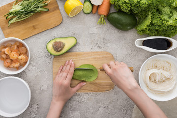 top view of woman cutting avocado with knife on cutting board