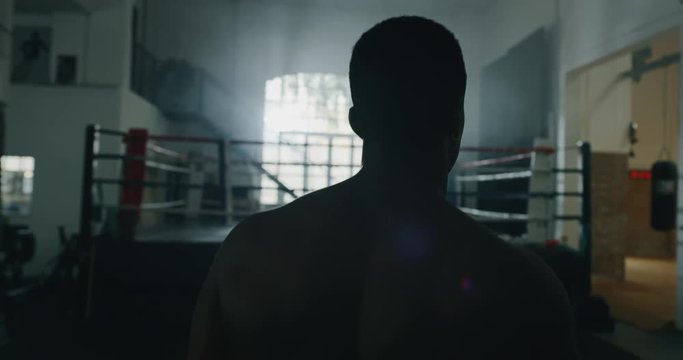 Cinematic slow motion back view shot of a professional young muscular shirtless african man is practicing shadow boxing work out in a ring. 