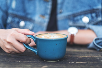Closeup image of a woman holding a blue cup of hot coffee on wooden table