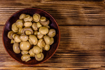 Ceramic plate with canned mushrooms on wooden table. Top view