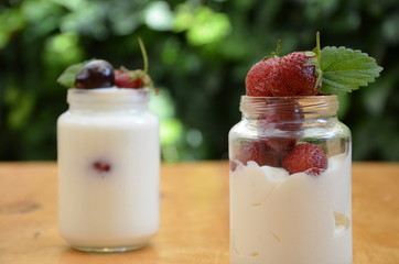 Healthy breakfast - granola, strawberries, cherry, honeysuckle berry, nuts and yogurt in a bowl. Vegetarian concept food. Top view. pudding or cocktail on the background of green foliage