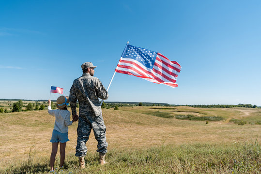 soldier holding hands with child and holding american flag