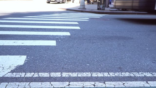 Yellow cab and other traffic going through an intersection in New York City, low angle shot focused on asphalt and crosswalk paint
