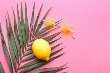 Stylish sunglasses with fresh lemon and tropical leaf on color background