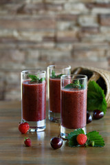 Smoothies of fresh cherries and strawberries in three glass glasses on the table in the country