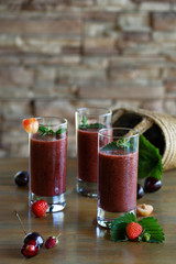 Smoothies of fresh cherries and strawberries in three glass glasses on the table in the country