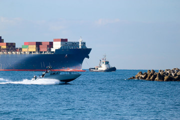 Coast guard boat on high speed in mediterranean sea with big gargo container ship and tugboat on the background