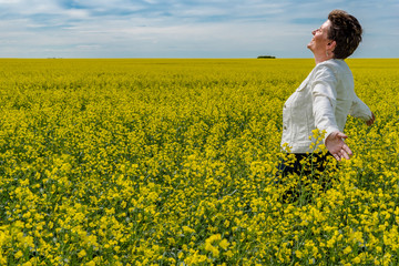 Fototapeta premium Young caucasian woman standing with arms raised in a canola field in bloom