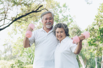 Cheerful elderly Asian man and senior Asian woman with dumbbell for workout in park, They smiling with good healthy together