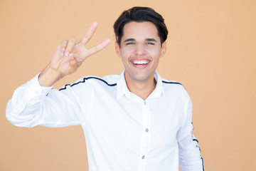 Happy handsome young man making victory gesture and looking at camera. Portrait of positive Latin guy showing two fingers. Success concept