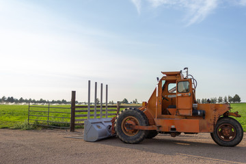 Side angle of orange tractor with a plow in a field with blue sky in the background
