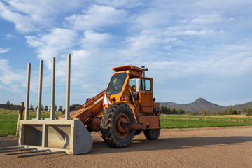 Side angle of orange tractor with a plow in a field with blue sky in the background