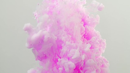 Isolated against a white background, mysterious pink liquid drops into clear water and slowly spreads and dissolves