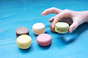 White child hand picking a colorful macaroon on blue background.