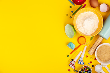 Baking birthday cupcakes ingredients on yellow background, flat lay
